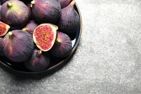 Whole and cut ripe figs on light gray textured table, top view. Space for text