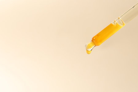 Dripping cosmetic serum from pipette on beige background, closeup. Space for textの写真素材