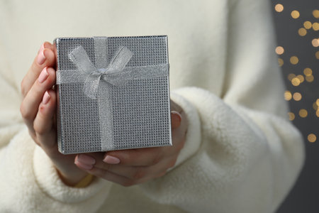 Christmas present. Woman holding gift box against gray background with blurred lights, closeupの写真素材