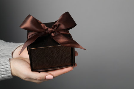 Christmas present. Woman holding gift box against gray background, closeup. Space for text