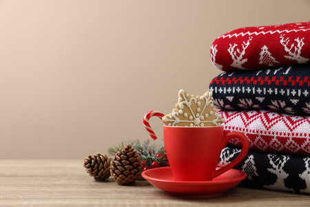 Stack of different Christmas sweaters, cup with candy cane, cookie and festive decor on wooden table, space for textの写真素材