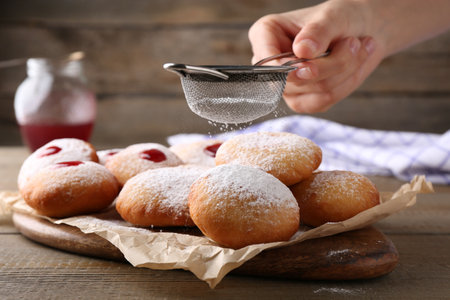 Woman dusting powdered sugar onto delicious Hanukkah donuts on wooden table, closeupの写真素材
