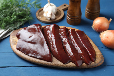 Cut raw beef liver with onions, garlic, dill and spices on blue wooden table, closeup
