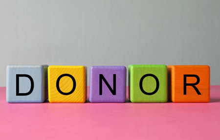 Word Donor made of colorful wooden cubes on pink tableの写真素材