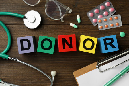 Word Donor made of colorful cubes, pills, clipboard and stethoscope on wooden table, flat layの写真素材