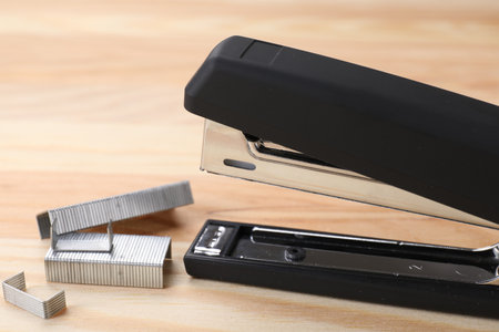 Black stapler with staples on wooden table, closeup
