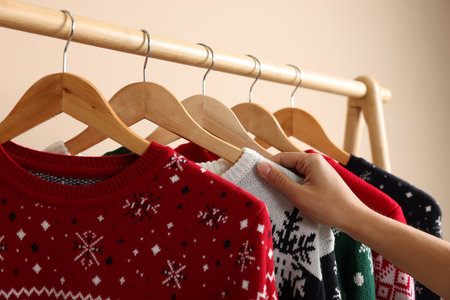 Woman choosing Christmas sweater from rack near beige wall, closeupの写真素材