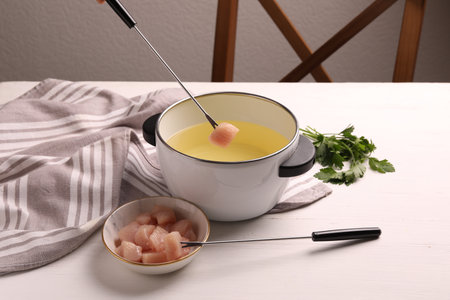 Dipping piece of raw meat into oil in fondue pot at white wooden tableの写真素材