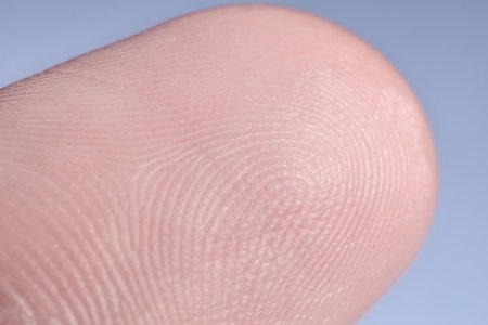 Finger with friction ridges on light blue background, macro view