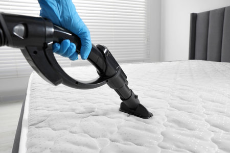 Person disinfecting mattress with vacuum cleaner indoors, closeupの写真素材