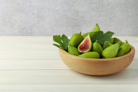 Cut and whole fresh green figs on white wooden table near gray wall, space for text