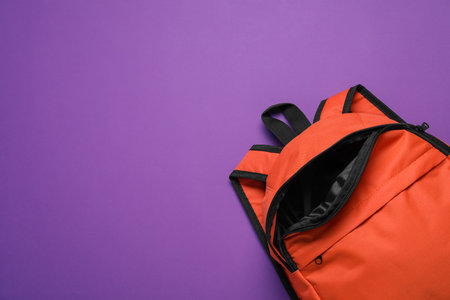 Stylish orange backpack on purple background, top view. Space for text