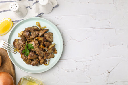 Tasty fried chicken liver with onion and parsley served on white textured table, flat lay. Space for textの写真素材