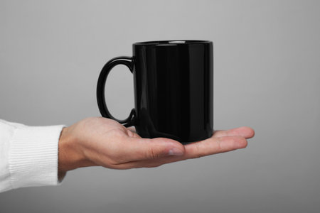 Man holding black mug on gray background, closeup