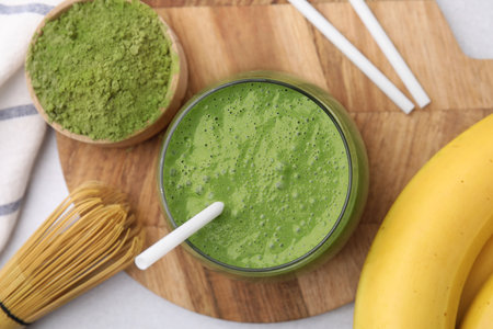 Glass of tasty matcha smoothie, powder, bamboo whiskey and banana on light table, flat layの写真素材