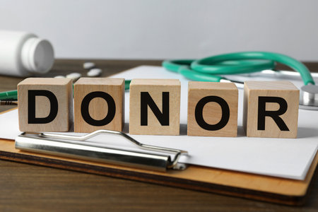 Word Donor made of cubes, clipboard and stethoscope on wooden table, closeupの写真素材