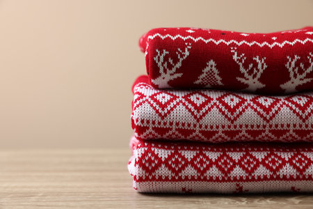 Stack of different Christmas sweaters on wooden table against beige background, closeup. Space for textの写真素材