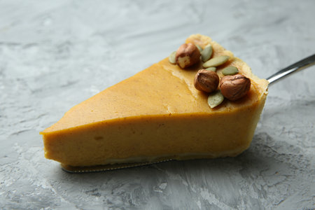 Cake server with piece of delicious pie with hazelnuts and pumpkin seeds on gray textured table, closeupの写真素材