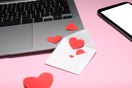 Long-distance relationship concept. Laptop, envelope with paper hearts and smartphone on pink background, closeupの写真素材