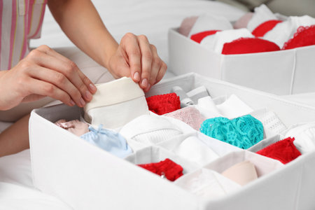 Woman putting underwear into organizer on bed, closeup