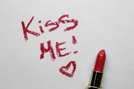 Phrase Kiss Me and red heart made with lipstick on white background, above viewの写真素材