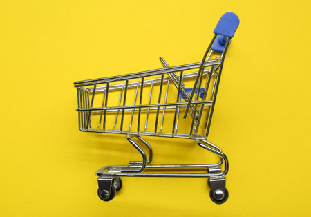 Small metal shopping cart on yellow background, top viewの写真素材