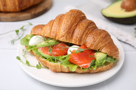 Tasty croissant with salmon, avocado, mozzarella and lettuce on white table, closeupの写真素材