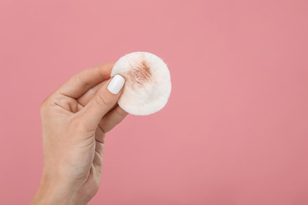 Woman with dirty cotton pad after removing makeup on pink background, closeup. Space for textの写真素材