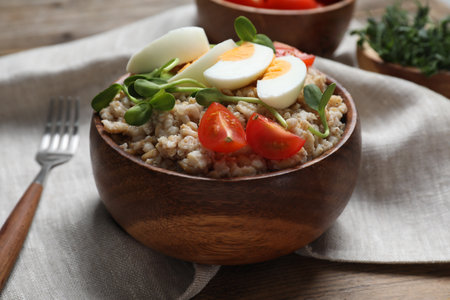 Tasty boiled oatmeal with egg, tomatoes and microgreens served on wooden table, closeupの写真素材