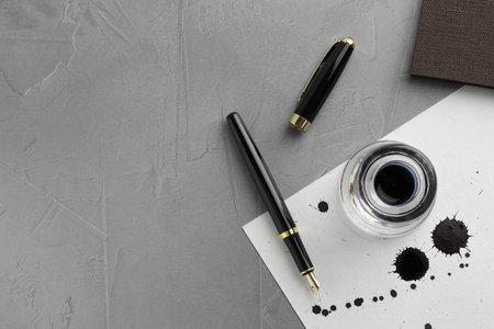 Stylish fountain pen, paper with blots of ink and inkwell on light gray textured table, flat lay....