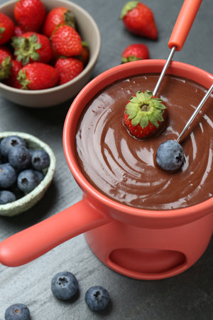 Dipping fresh berries in fondue pot with melted chocolate at gray table, above viewの写真素材