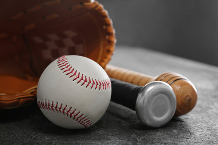 Baseball bats, glove and ball on gray table, closeup
