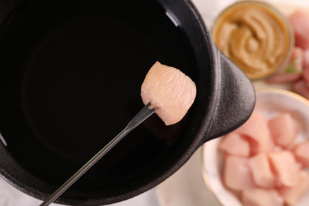 Fondue pot with oil, fork, raw meat piece and mustard on white table, flat layの写真素材