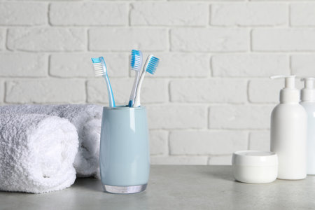 Plastic toothbrushes in holder, cosmetic products and towels on light gray table. Space for textの写真素材