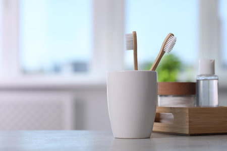 Bamboo toothbrushes in holder and cosmetic products on light gray table. Space for textの写真素材