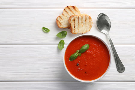 Delicious tomato cream soup in bowl served with pieces of grilled bread on white wooden table, flat lay. Space for textの写真素材