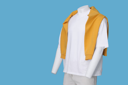 Male mannequin dressed in white t-shirt, stylish shorts and orange sweater on light blue background,...