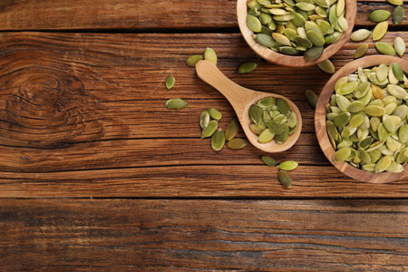 Bowls and spoon with peeled pumpkin seeds on wooden table, flat lay. Space for textの写真素材