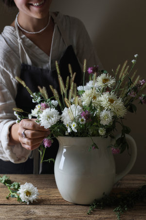 Smiling woman creating beautiful flower arrangement at wooden table, closeup
