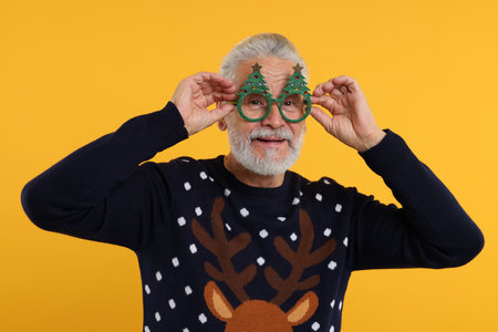 Senior man in Christmas sweater and funny glasses against orange backgroundの写真素材