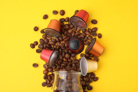 Many coffee capsules, beans and glass jar on yellow background, flat layの写真素材