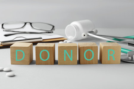 Word Donor made of wooden cubes, clipboard, pills and stethoscope on light gray tableの写真素材