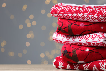 Stack of different Christmas sweaters on table against gray background with blurred lights. Space for textの写真素材