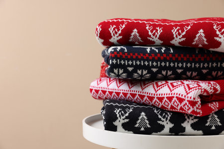 Stack of different Christmas sweaters on white table against beige background, closeup. Space for textの写真素材