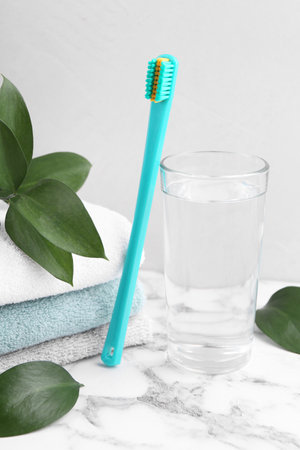 Plastic toothbrush, glass of water, towels and green leaves on white marble tableの写真素材