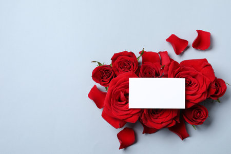 Blank card, beautiful red roses and petals on gray background, top view. Space for textの写真素材