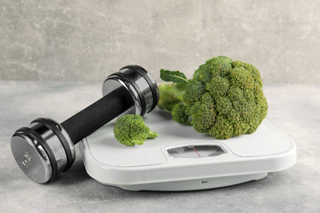 Healthy diet. Scale, broccoli and dumbbell on gray tableの写真素材