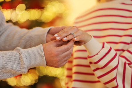 Making proposal. Man putting engagement ring on his girlfriend's finger against blurred lights, closeupの写真素材