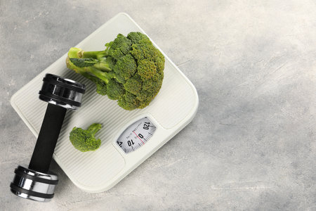 Healthy diet. Scale, broccoli and dumbbell on gray table, top view. Space for textの写真素材