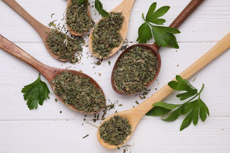 Spoons with dried aromatic parsley and fresh leaves on white wooden table, flat layの写真素材
